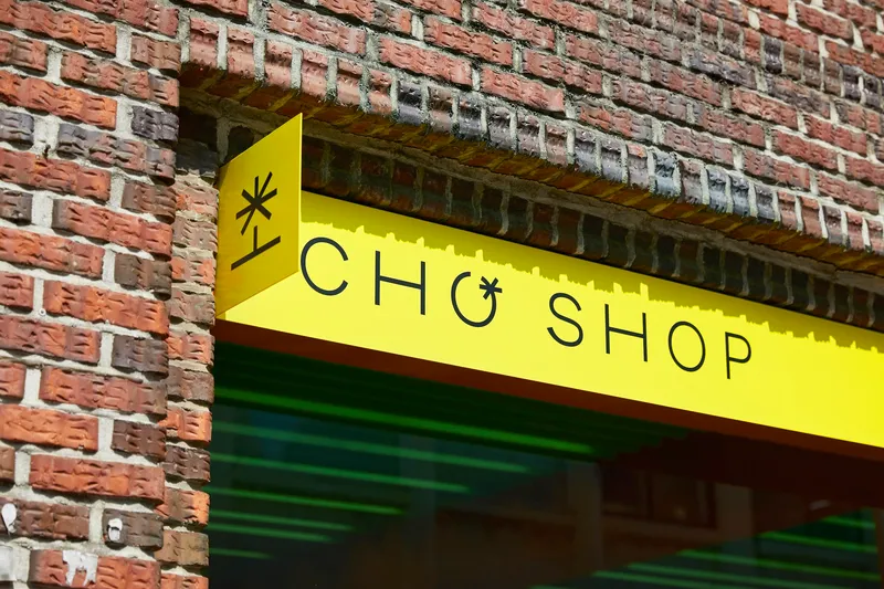 Yellow signage blade projecting from weathered brick facade with geometric mortar pattern