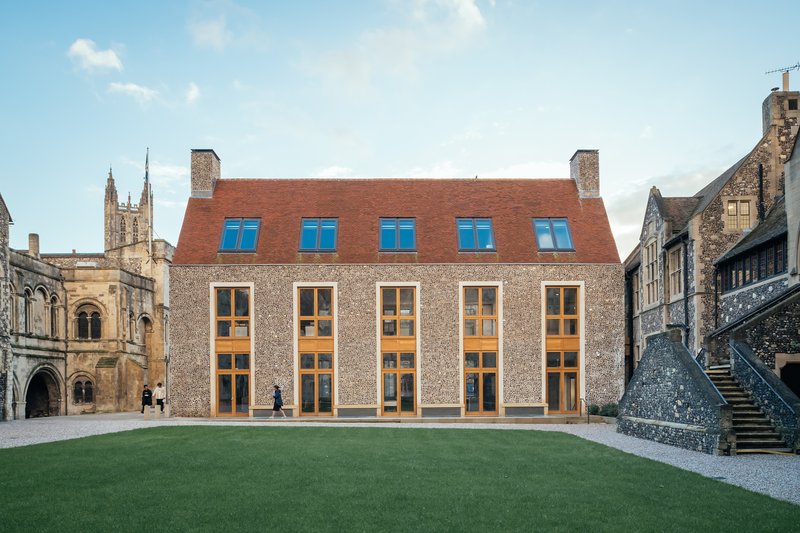 Flint facade with timber-framed windows and a red clay tile roof facing a gravel courtyard