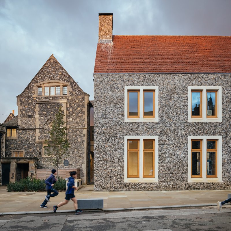 Flint wall with timber-framed windows facing the street as students walk past in the foreground