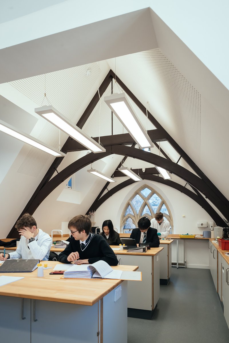 Interior space with exposed timber trusses and a gothic arched window where students work at benches
