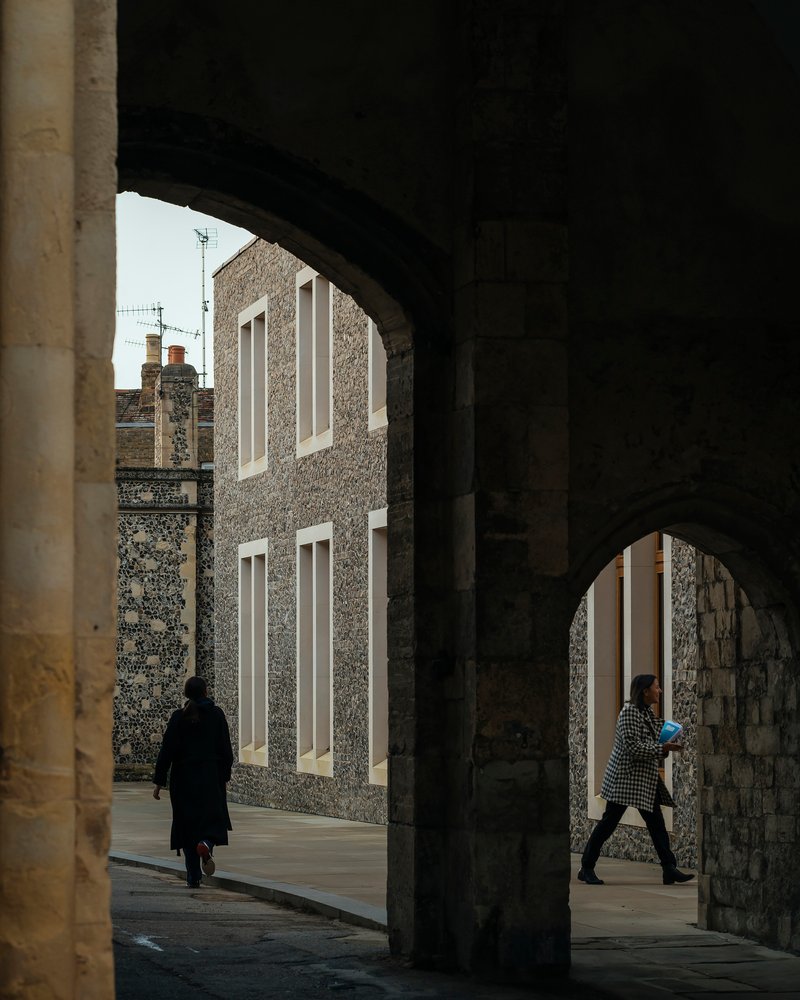 View through a vaulted passage showing the flint facade and two figures walking in opposite directions