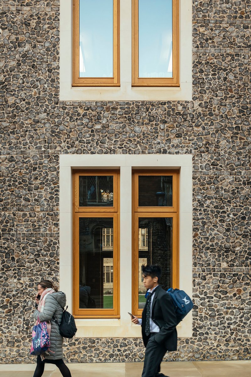 Cobblestone facade with timber-framed windows and two students walking past beneath sunny skies