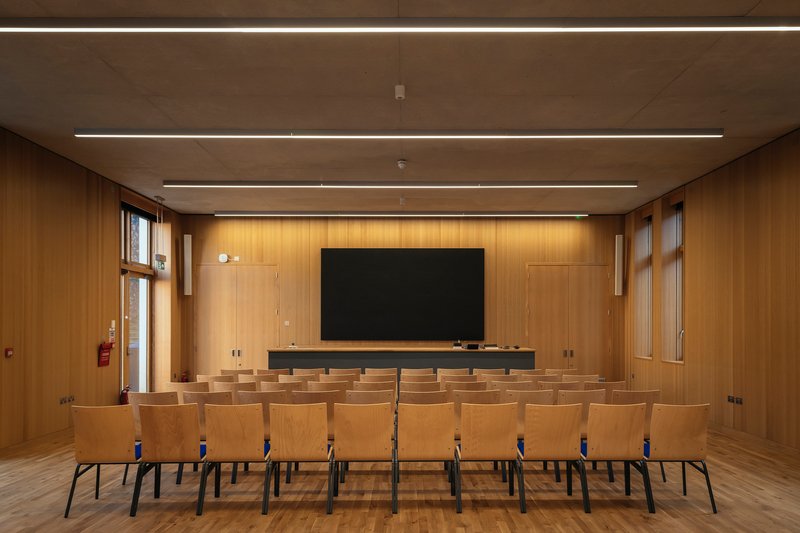 Assembly hall with timber-paneled walls, rows of chairs and recessed linear lighting overhead