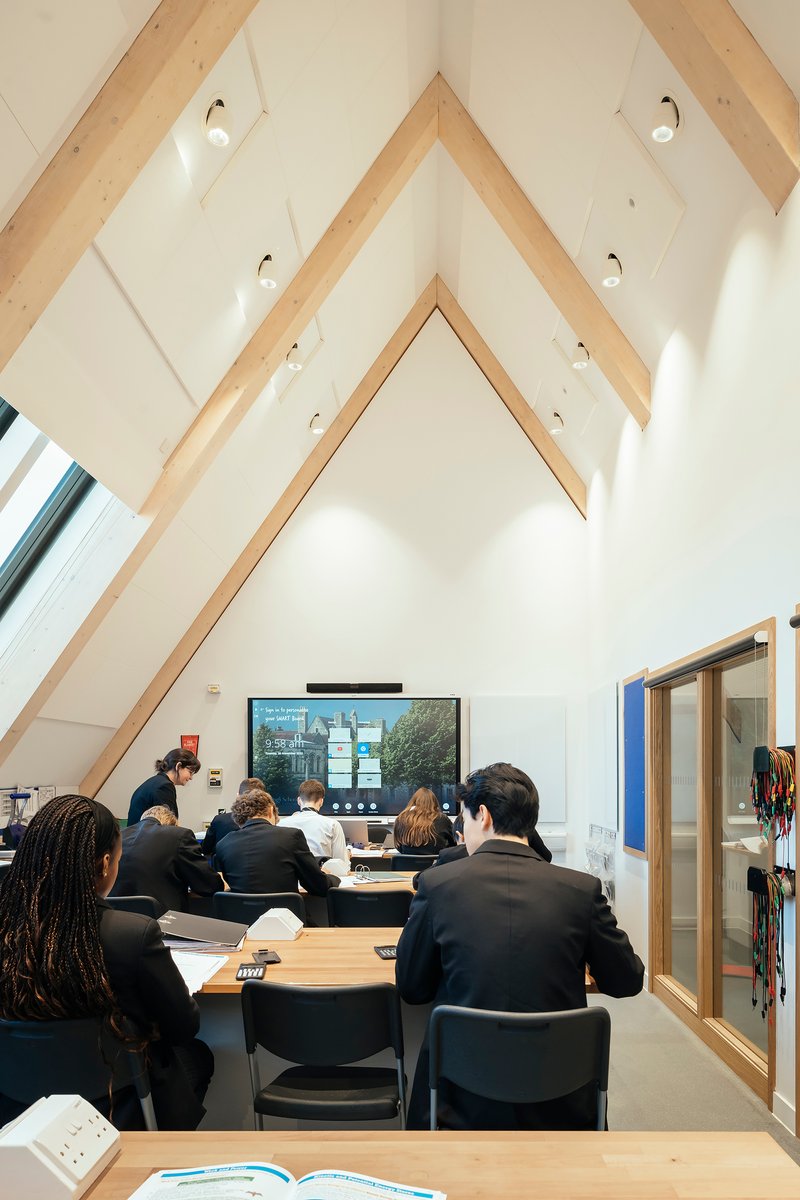 Classroom beneath exposed timber trusses with students seated around a table under skylight