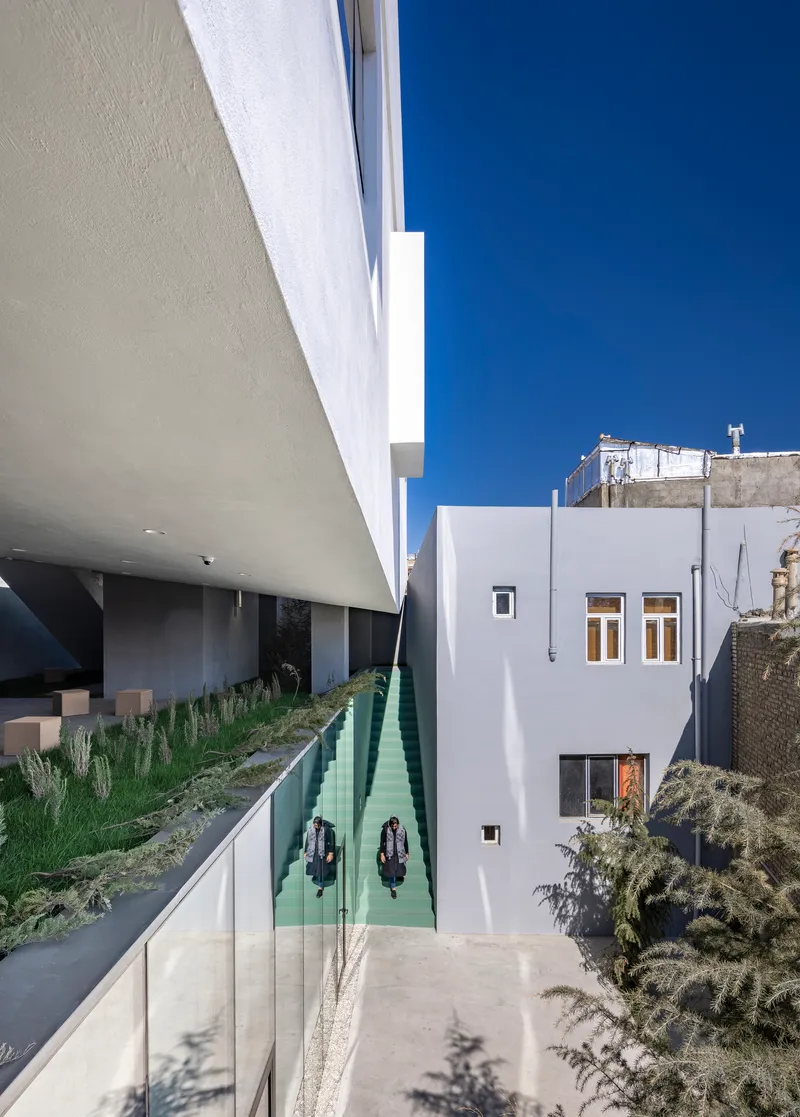 Entry courtyard with mint green reflecting pool beneath a cantilevered white volume in bright sunlight