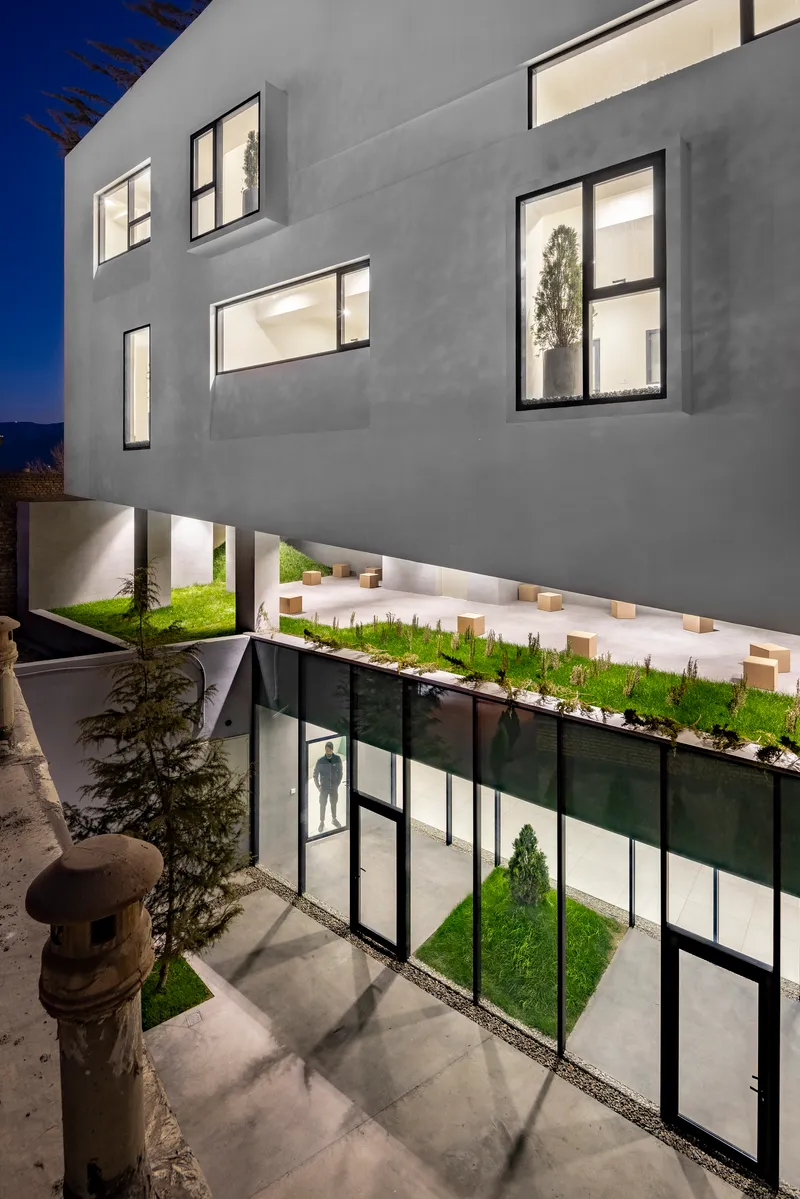 Planted courtyard with glazed walls below cantilevered white volumes at blue hour