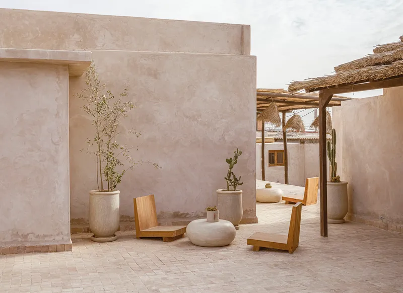 Courtyard corner with timber lounge chairs and potted plants beneath a thatched pergola in soft light