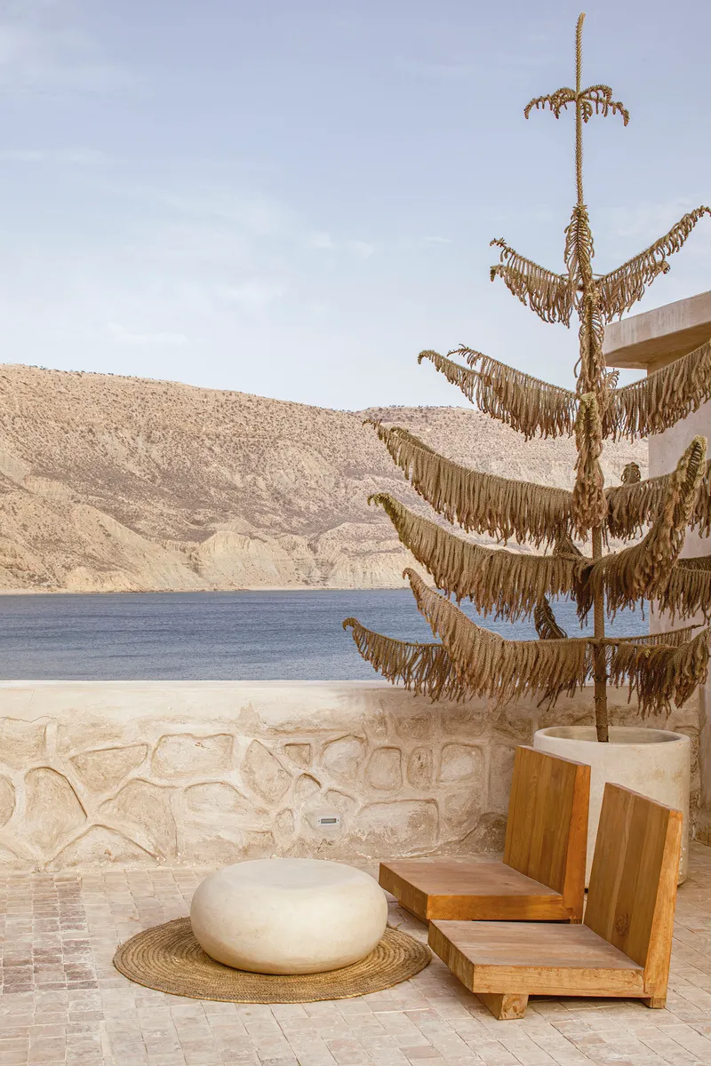 Terrace with decorative rope sculpture on pole beside stone seat wall overlooking water and hills