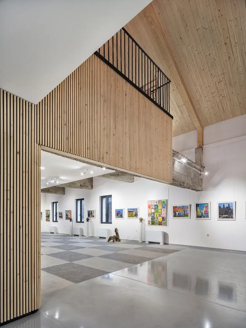 Gallery interior with polished tile flooring and timber-clad mezzanine volume projecting into the space