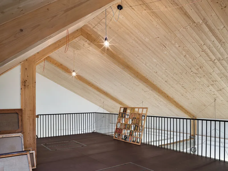 Gabled timber-lined attic workspace with exposed rafters and pendant lights above a metal railing