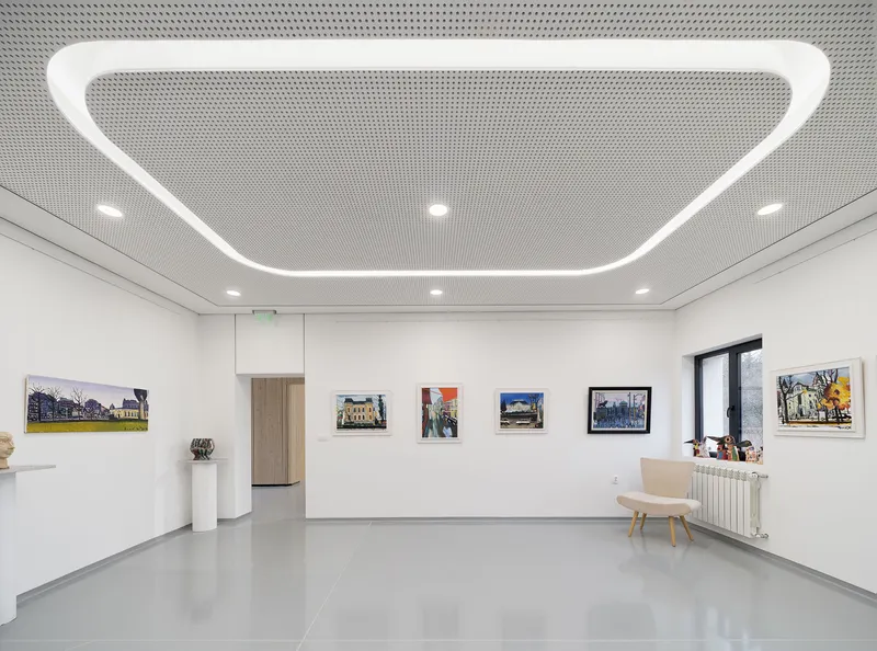 Gallery space with white walls displaying framed artworks and a curved linear ceiling light