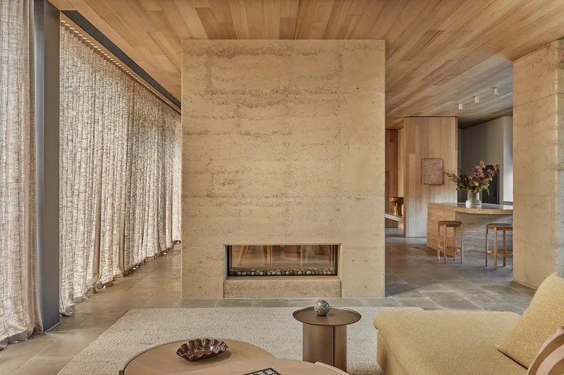 Rammed earth fireplace wall with linen curtains and view through to dining area beyond
