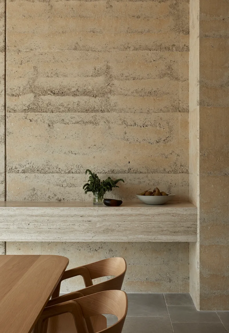 Built-in rammed earth bench with potted plant and fruit bowl against horizontal grain wall