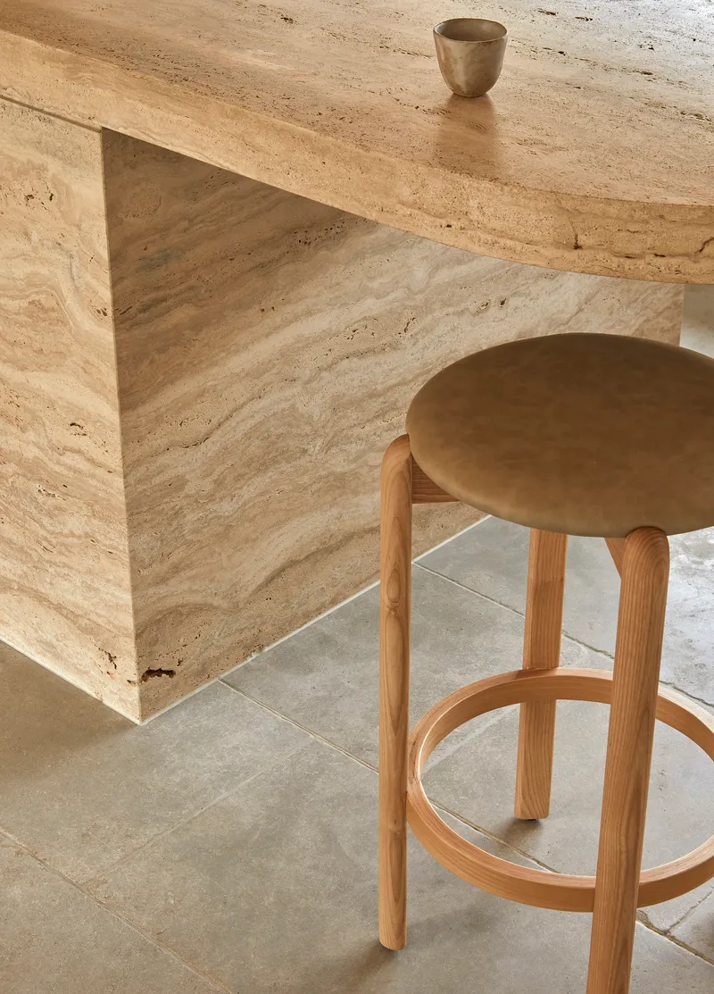 Close-up of travertine island bench meeting a timber stool with exposed leg joinery