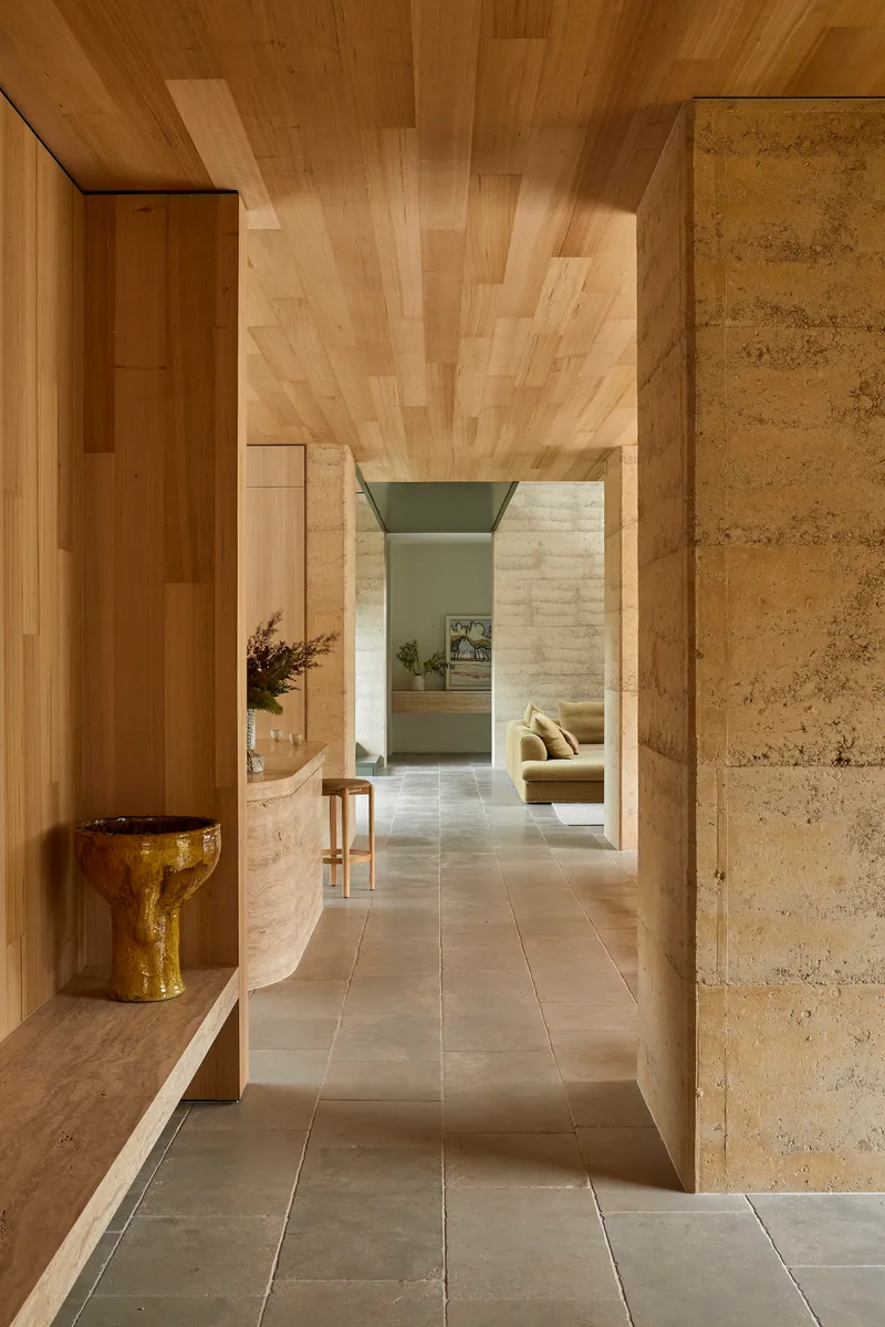 Hallway with timber ceiling planks, rammed earth walls and curved bench with ceramic vessel