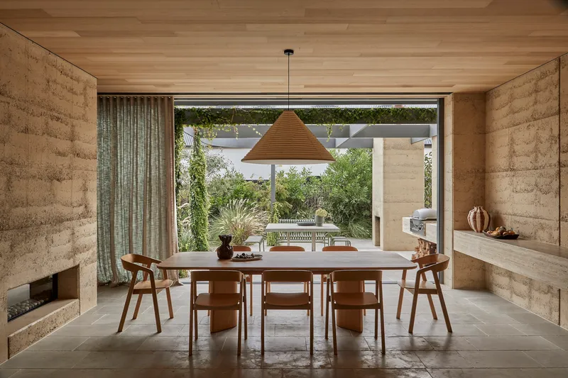 Dining room with rammed earth walls and timber ceiling opening to a planted courtyard