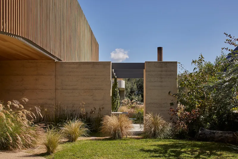 Rammed earth walls framing a courtyard with ornamental grasses under clear sky