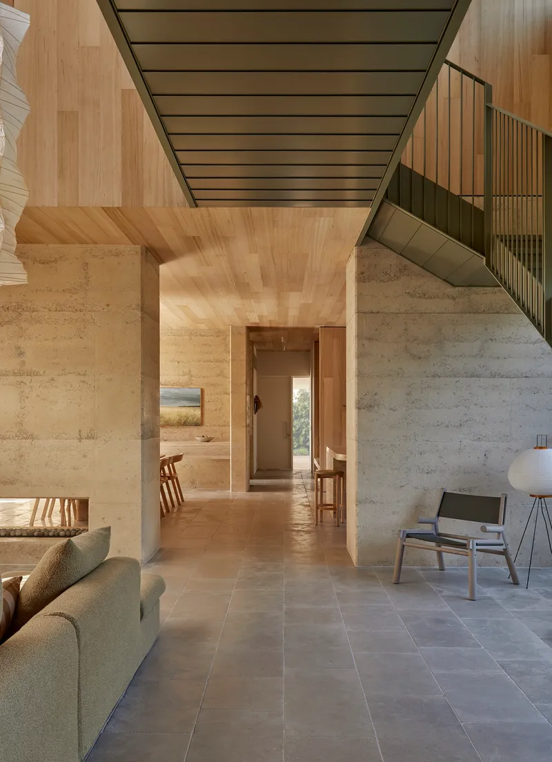 Interior corridor with rammed earth column, timber ceiling and view through to distant doorway