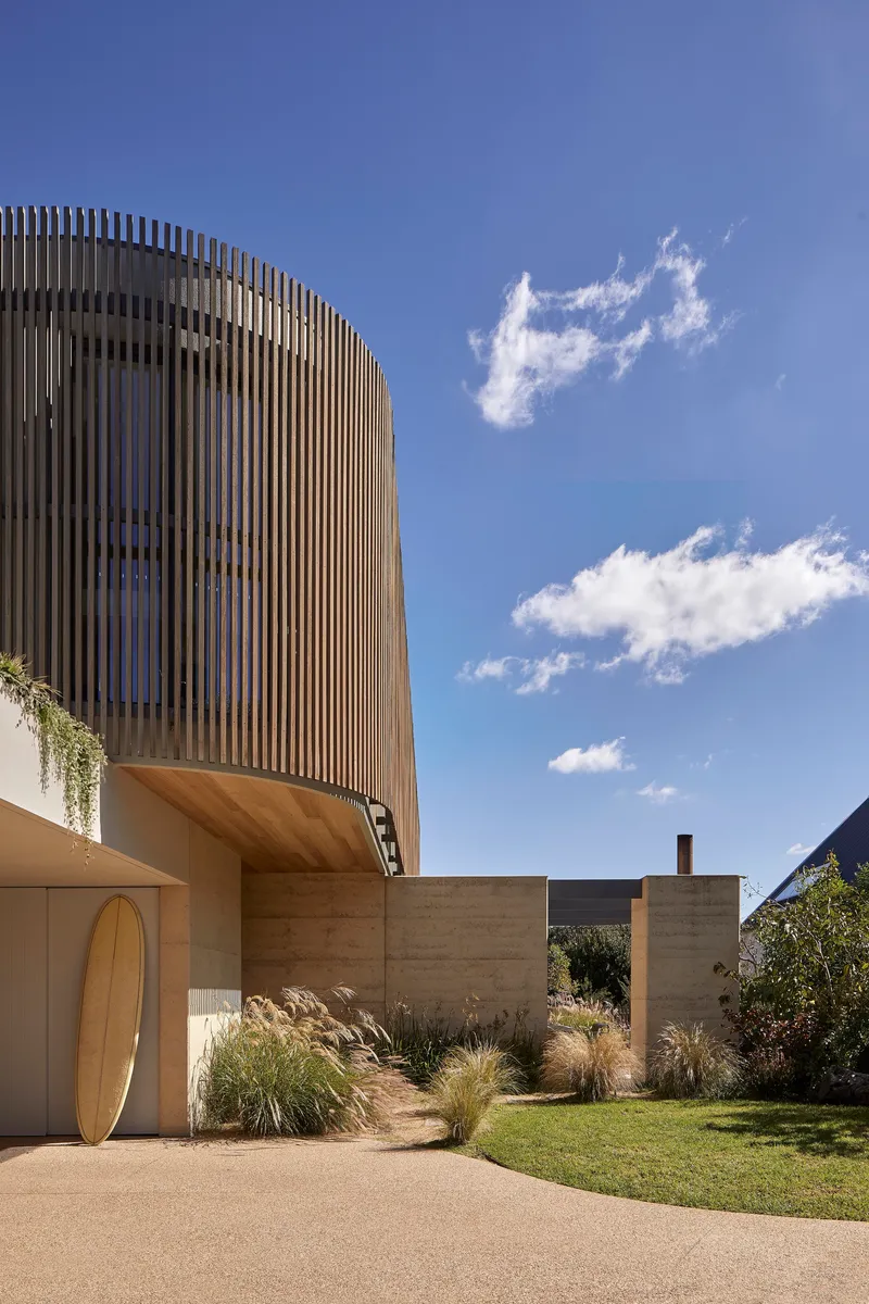 Two-storey facade with vertical timber screening above rammed earth walls and planted garden beds