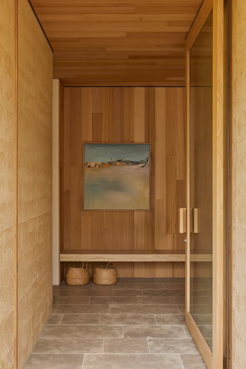 Entry vestibule with timber-lined walls and ceiling leading to a bench with woven baskets below