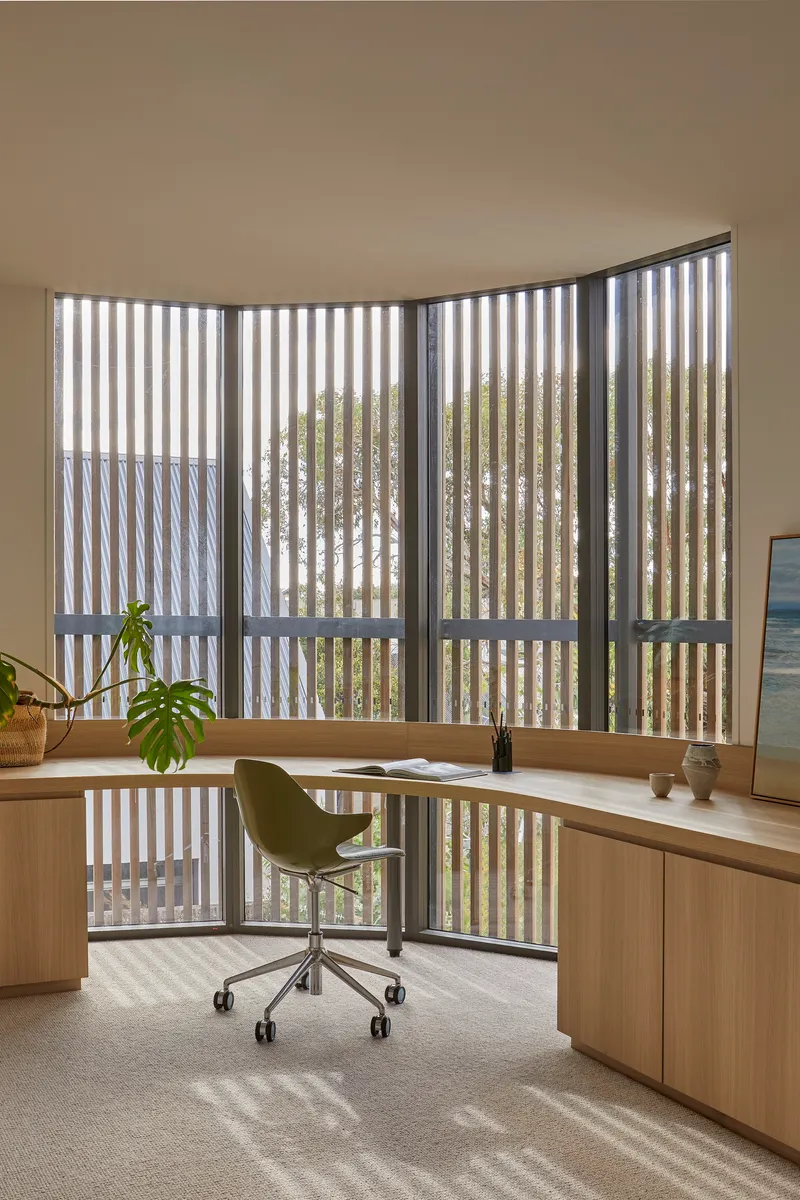Curved study desk at a vertical timber screen filtering dappled light onto the workspace