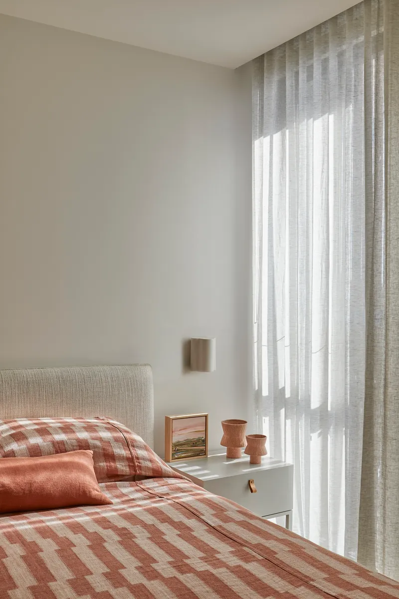 Bedroom corner with sheer linen curtains filtering soft daylight onto white walls