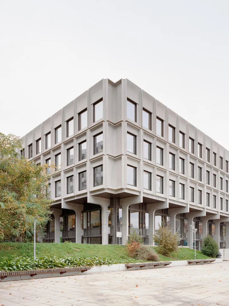 Corner elevation showing precast facade on piloti with grass slope in foreground