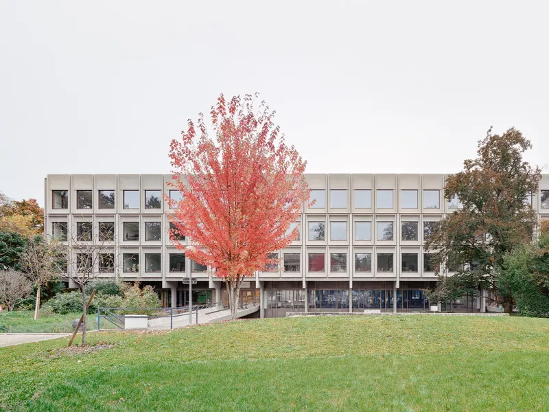 View of the concrete framed facade across a lawn with a red-leafed tree in autumn