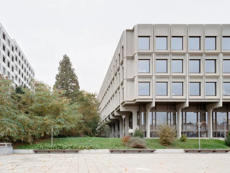 Corner view of the precast concrete facade on pilotis with paved plaza in foreground