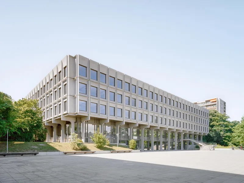 Long view of the elevated concrete structure on pilotis with paved forecourt
