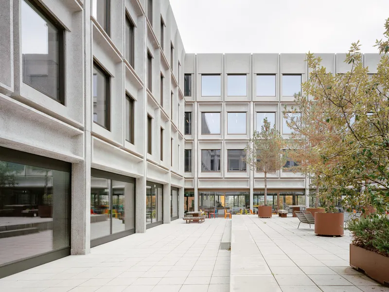 Central courtyard with paved terrace, planted beds in corten planters, and surrounding concrete grid facades