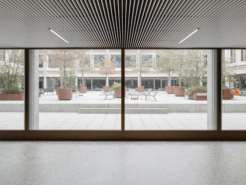 Interior view through bronze-framed glazing overlooking the courtyard with slatted wood ceiling overhead