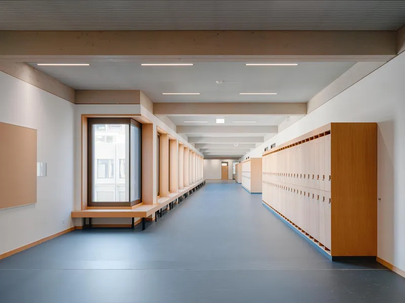 Corridor with wooden locker wall, continuous bench seating, and exposed concrete ceiling beams with linear lighting