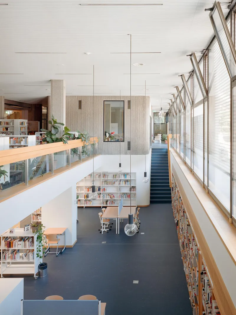 Double-height library space with sawtooth clerestory windows, timber shelving, balconies and dark flooring below