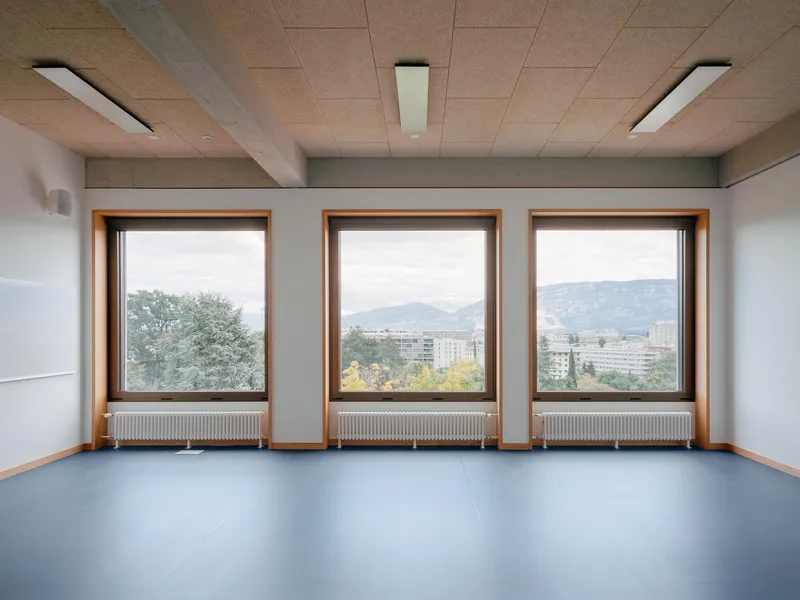 Empty room with three timber-framed windows overlooking distant mountains and residential blocks in overcast weather