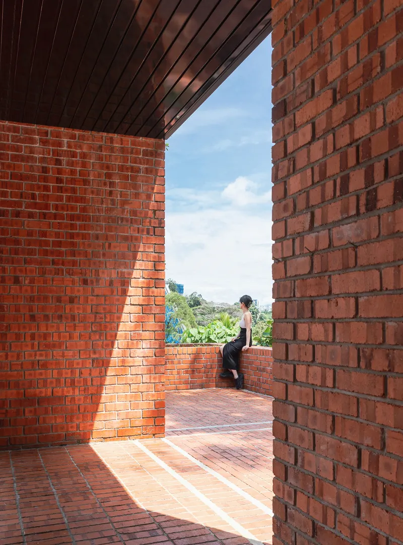 Framed view through brick walls to terrace where a figure stands looking toward vegetation