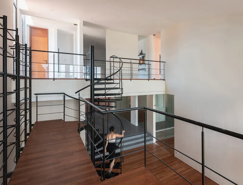 Black steel spiral staircase connecting multiple levels with horizontal railings and wood flooring