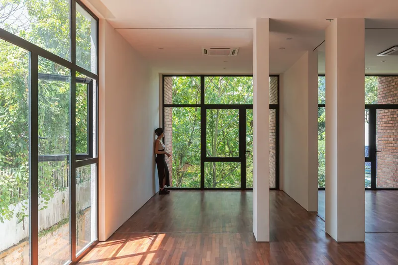 Double-height interior space with black-framed windows overlooking green foliage and a person standing