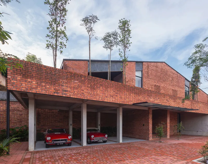 Covered carport with concrete columns beneath red brick facade and rooftop garden with tall trees