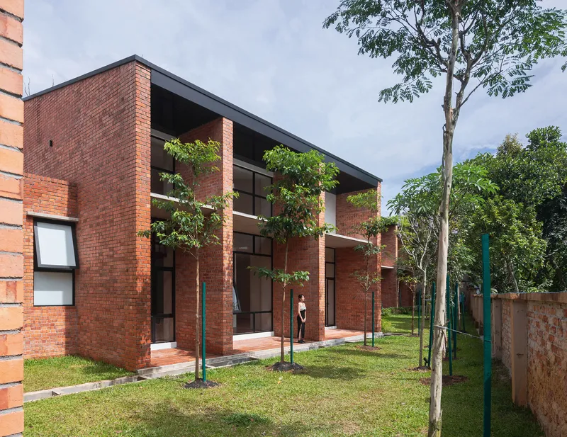 Rear facade with tall glazed openings framed by brick piers in a garden with young trees