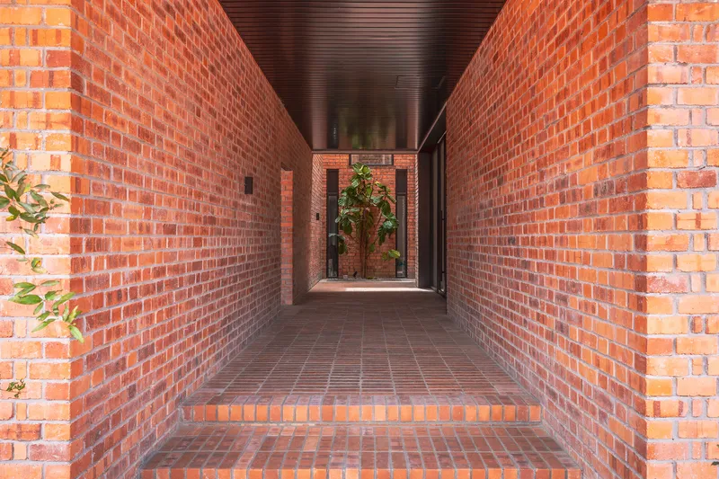 Narrow brick corridor with timber ceiling leading to a planted courtyard at the far end