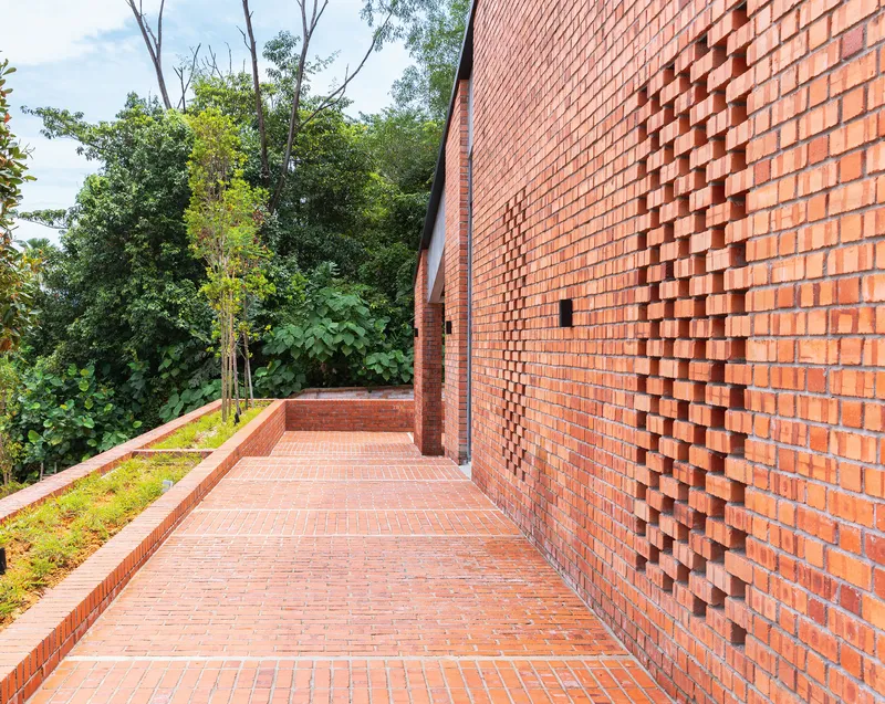 Red brick paved terrace with textured projecting brick wall pattern alongside planted bed and trees