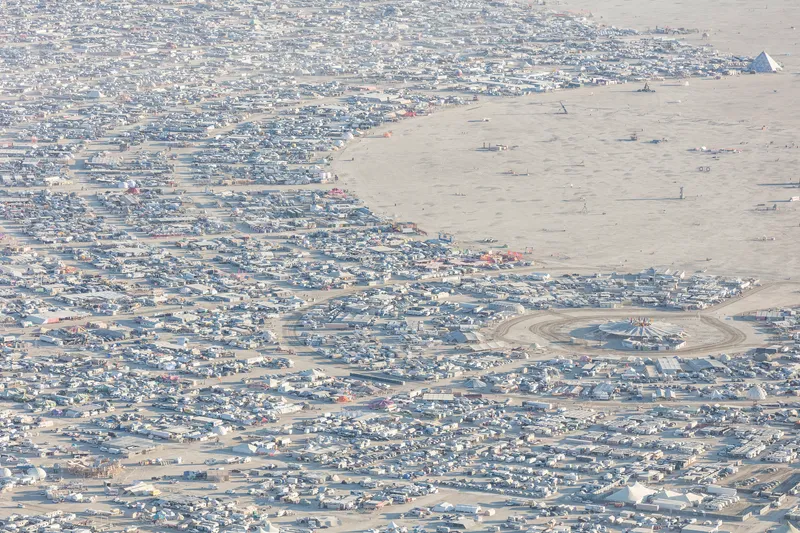 Aerial view of temporary encampment scattered across desert with curving pathways and central installations