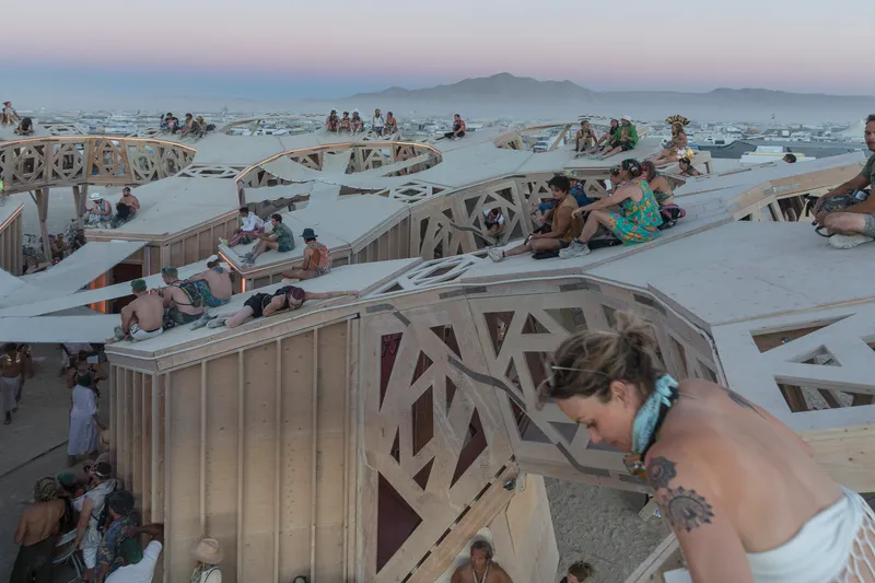 Visitors resting on tiered timber platforms with patterned parapets at twilight with mountains beyond