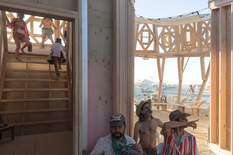 Timber staircase and elevated platform with geometric patterned screens, visitors climbing and gathering below