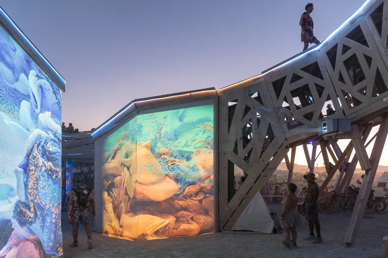 Exterior facade with backlit translucent panels showing swirling imagery beneath latticed timber canopy