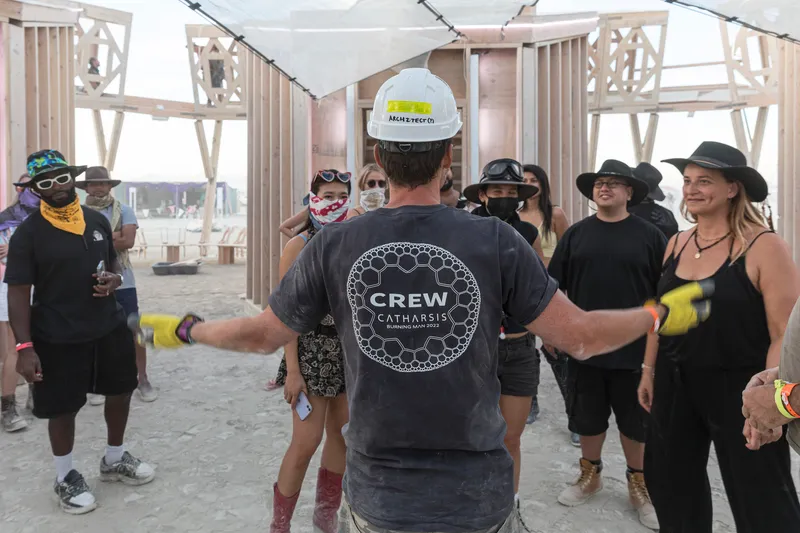 Interior gathering space with timber frame structure and fabric ceiling during a guided tour
