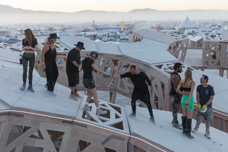 Rooftop deck with angled timber trusses and visitors gathered at dusk overlooking distant mountains