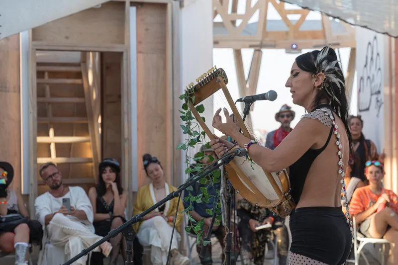 Interior view of an exposed timber frame structure with a performer and seated audience during a daytime gathering