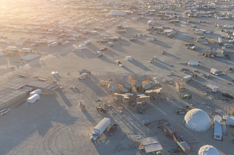 Drone view of a radial timber installation surrounded by temporary structures and vehicles in a sandy terrain